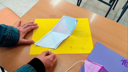 Animación de una red plana de triángulos de papel que, al tirar de un hilo central, se eleva y ensambla formando un icosaedro tridimensional